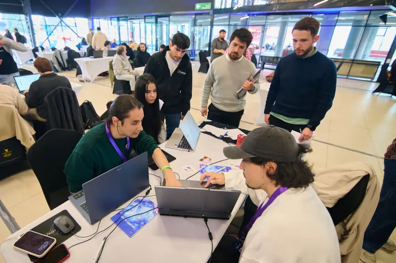 Varias personas de pie conversan alrededor de la mesa del equipo, entre computadores y material del evento.