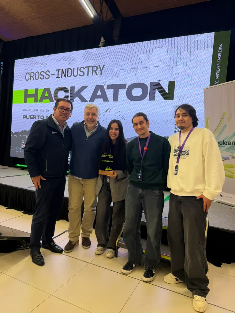 El equipo de ProGarLabs, con el galardón de ganador, junto a dos personas frente a la pantalla de la Cross-Industry Hackaton.