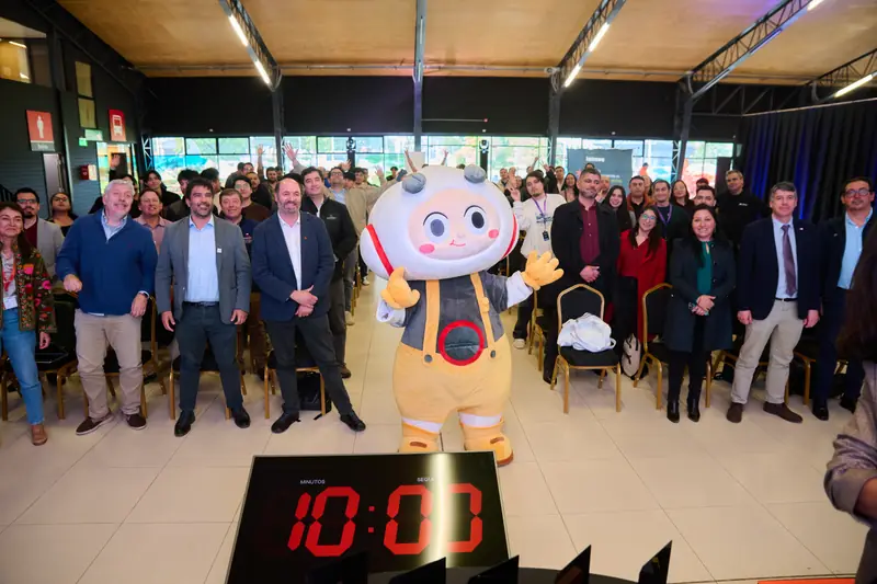 Participantes y la mascota del evento reunidos en el salón principal, con un reloj de cuenta regresiva en primer plano.